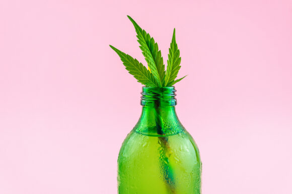 Green glass bottle with Cannabis CBD infused Water lemonade with cannabis leafs isolated on pink